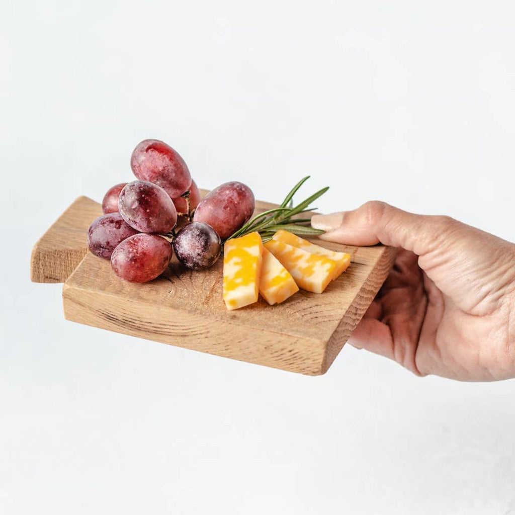 Handing reaching out to show small wooden charcuterie board with grapes, cheese and herbs