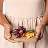 Small wooden tray held by two hands topped with grapes, cheese and herbs