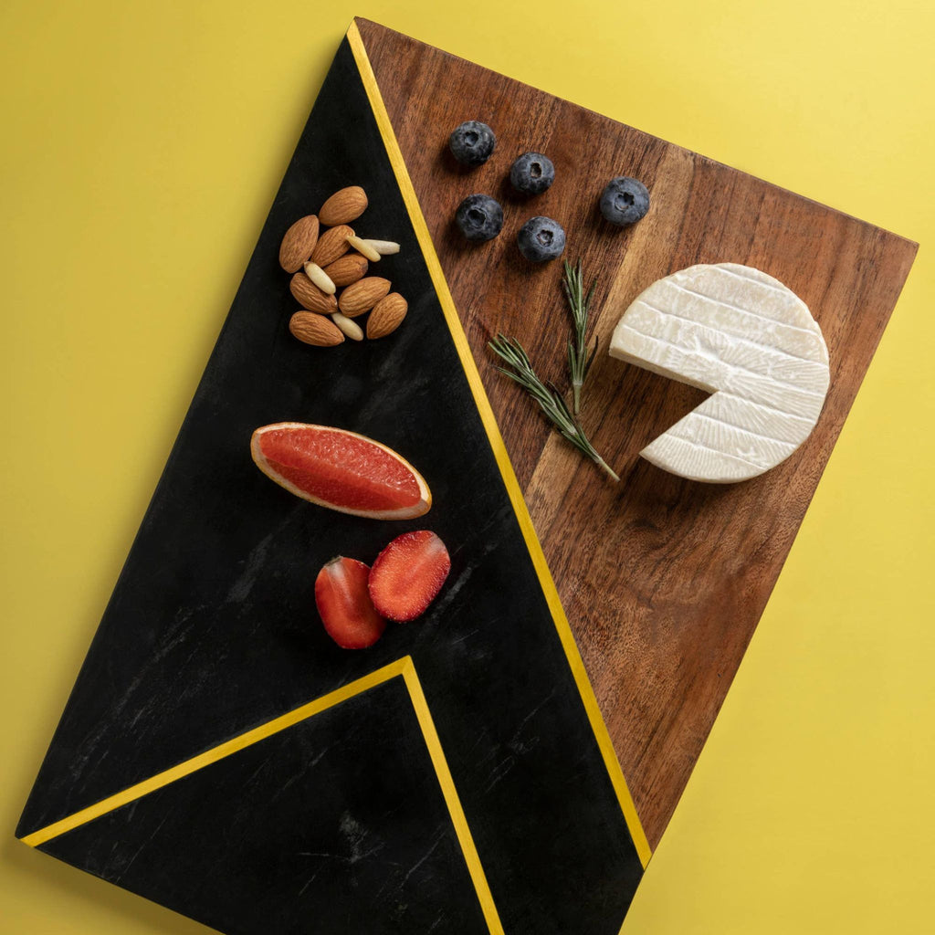 Black marble and wood tray with brass inlay topped with brie, nuts, fruit and herbs